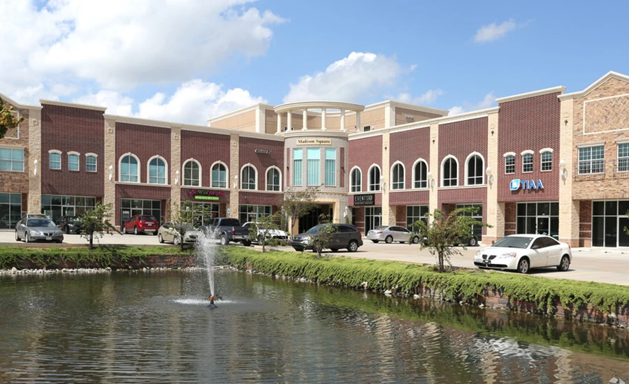 shopping center with brick buildings behind a small pond with a water fountain